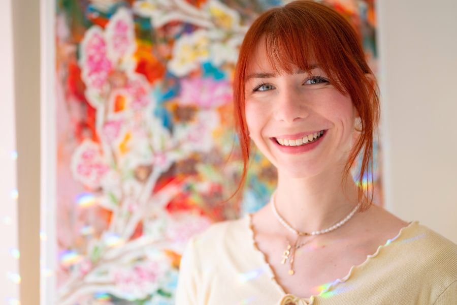 Portrait von La'inesh (Nadine Christel) mit einem bunten Bild im Hintergrund.